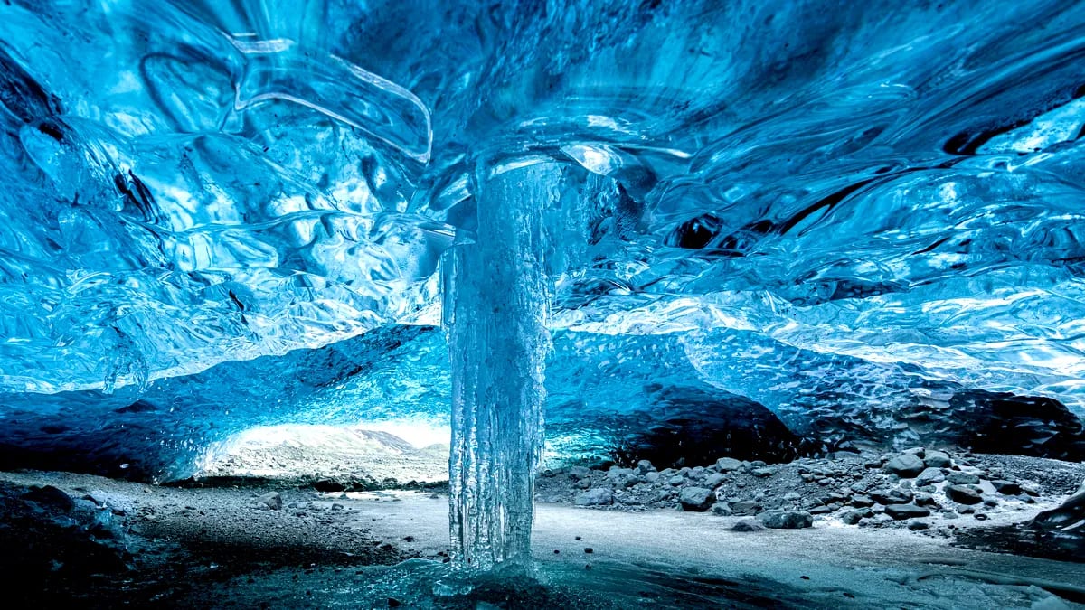 Blue ice cave beneath an Icelandic glacier with crystal ice ceiling, frozen pillar and rocky floor, a dramatic May adventure in Iceland