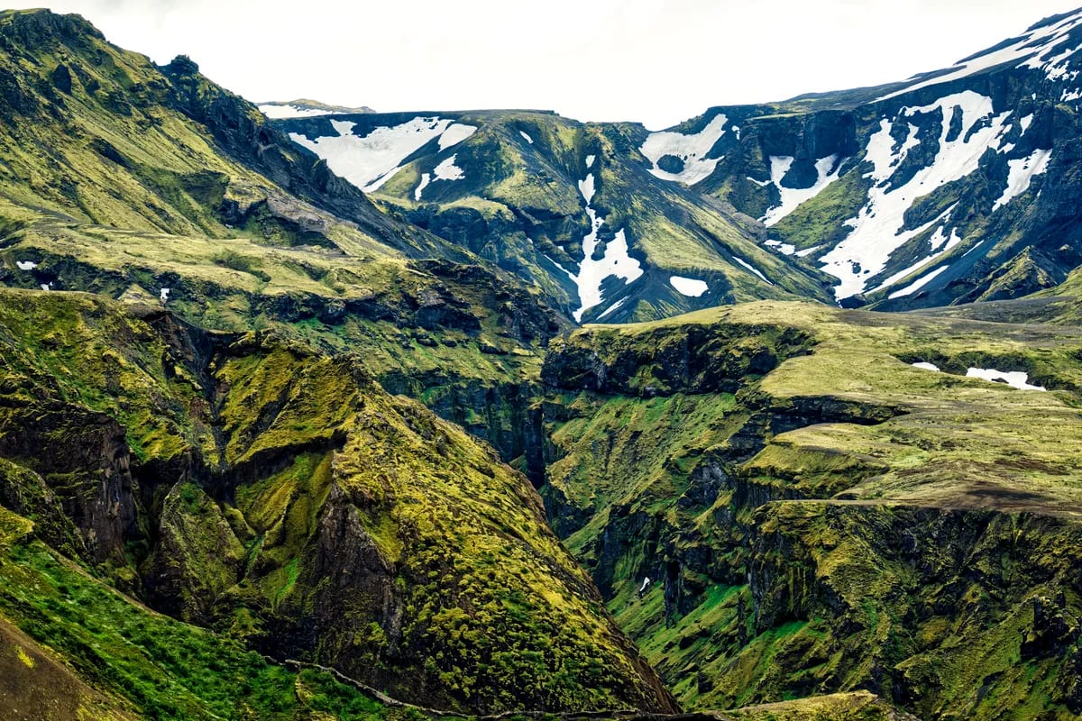 Green Icelandic highland canyon in June with mossy volcanic cliffs, rugged ridges, snow patches, and dramatic mountain slopes.