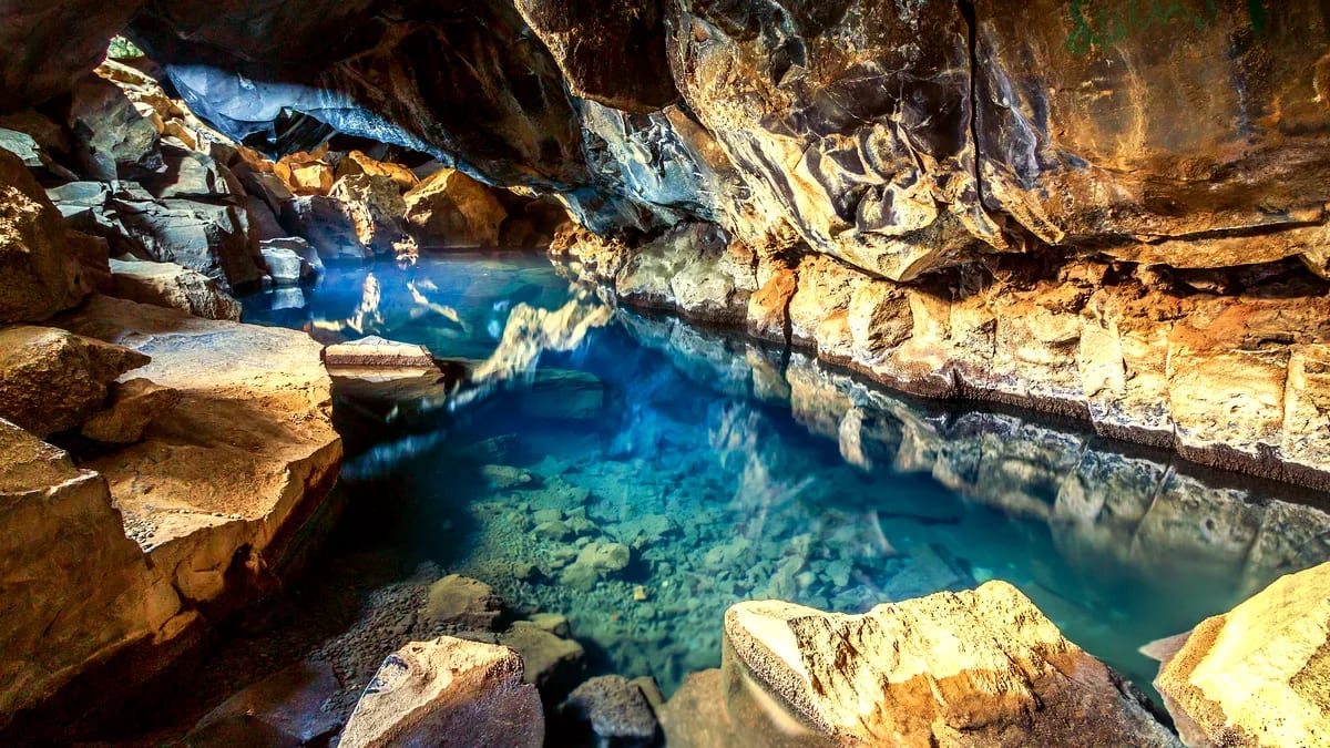 Grjótagjá lava cave in Iceland with clear blue geothermal water, rocky walls, warm reflections, and hidden summer travel vibes in June.