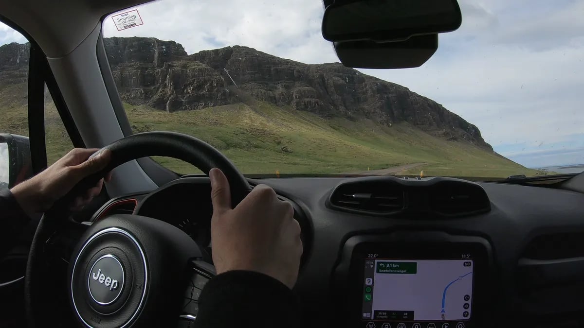 Driver’s view from a Jeep road trip in Iceland in June, passing steep cliffs, green hills, navigation map, and open scenic highway.