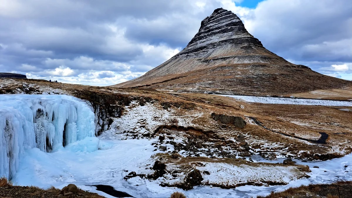 Frozen Kirkjufellsfoss waterfall beneath snow-dusted Kirkjufell mountain, with icy cliffs and dramatic winter clouds in Iceland