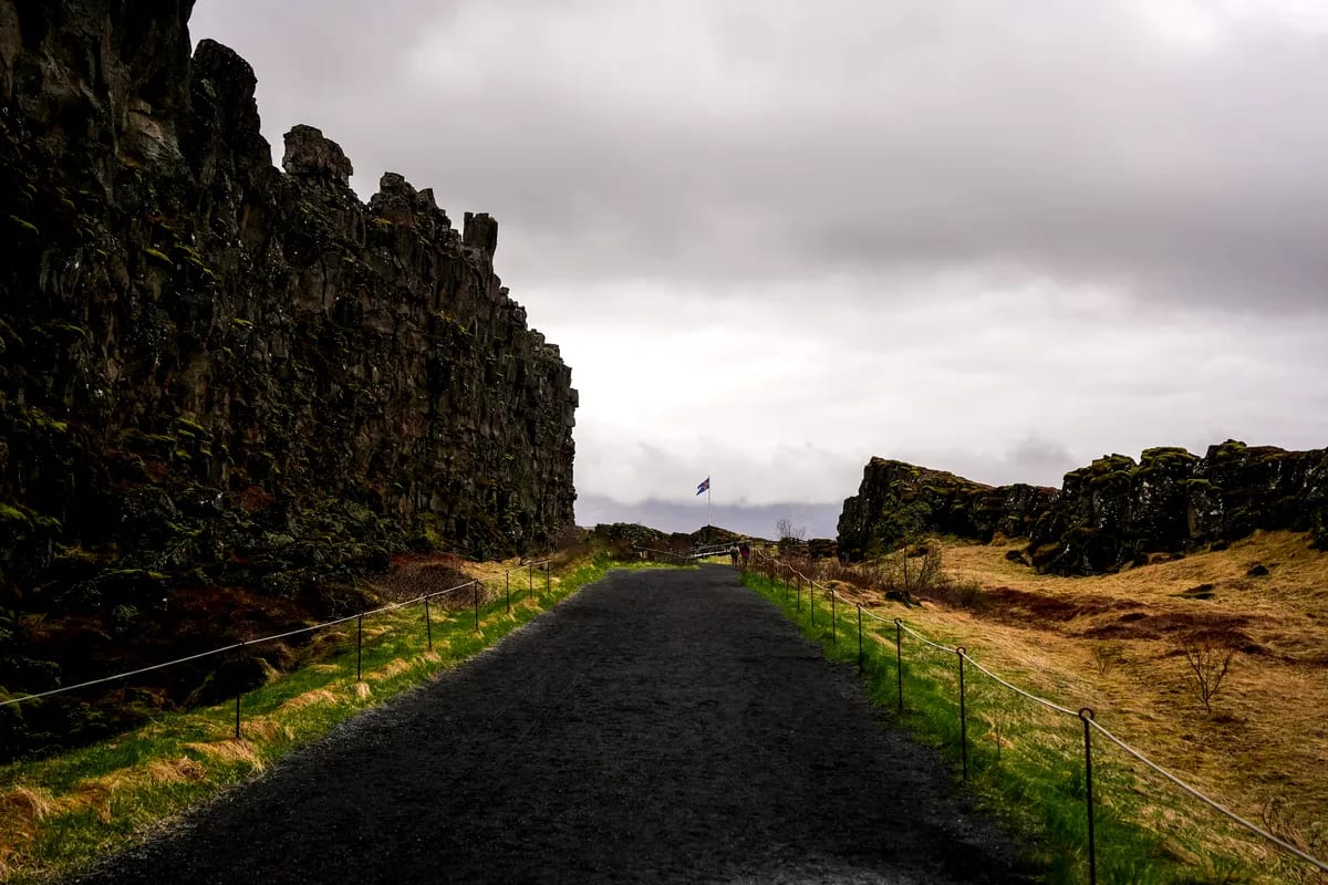 Path through Almannagjá rift at Thingvellir National Park in Iceland, framed by mossy lava cliffs, cloudy April skies, and a volcanic trail