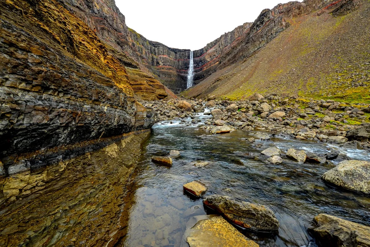 Hengifoss Waterfall rising above a rocky river canyon with red clay bands, basalt cliffs and mossy slopes on Iceland’s Eastfjords trail