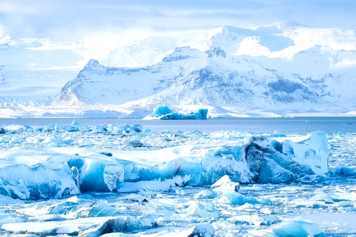 Blue icebergs float across Iceland’s glacier lagoon in January, with snow-covered mountains and frozen shoreline glowing in bright winter light