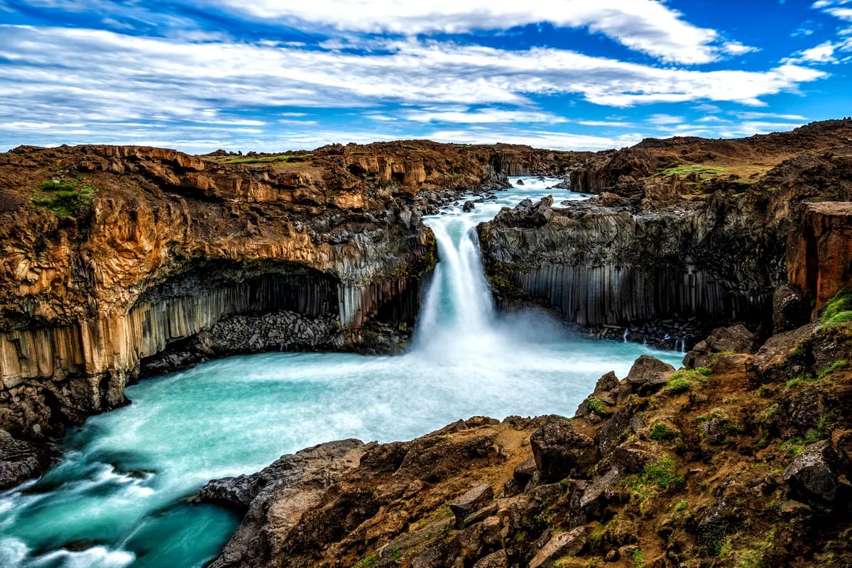 Aldeyjarfoss waterfall pouring into a turquoise pool, framed by rugged basalt columns and volcanic cliffs under a dramatic Iceland sky