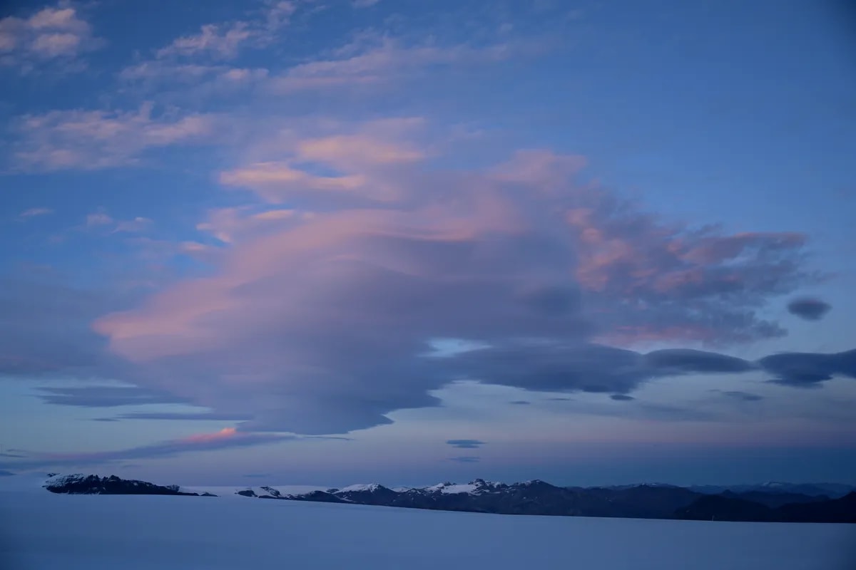 Blue winter twilight over an Icelandic fjord in December, with pink clouds, calm water, distant snowy islands and rugged mountains