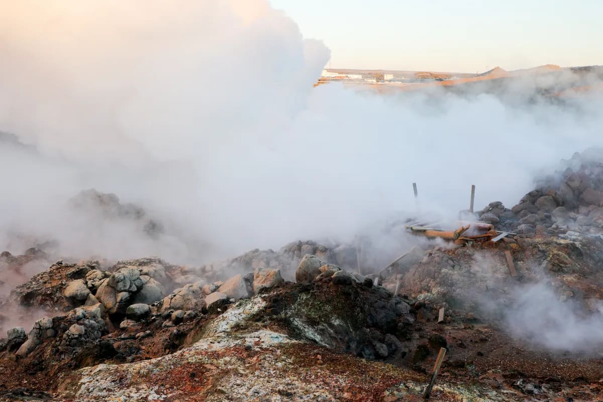 Steaming geothermal field in Iceland with rocky mineral ground, thick white vapor from hot springs and soft winter light in December