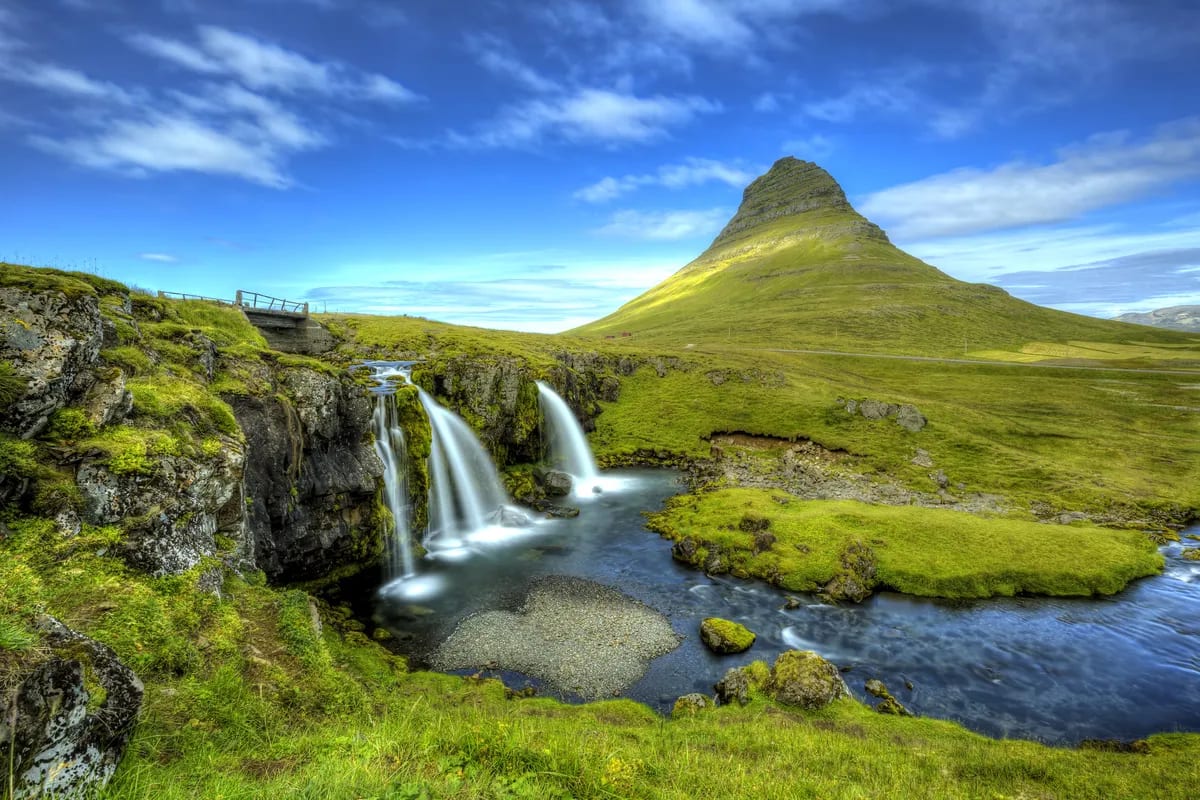 Kirkjufell mountain and Kirkjufellsfoss waterfall on Iceland’s Snæfellsnes Peninsula, with green mossy cliffs and blue sky