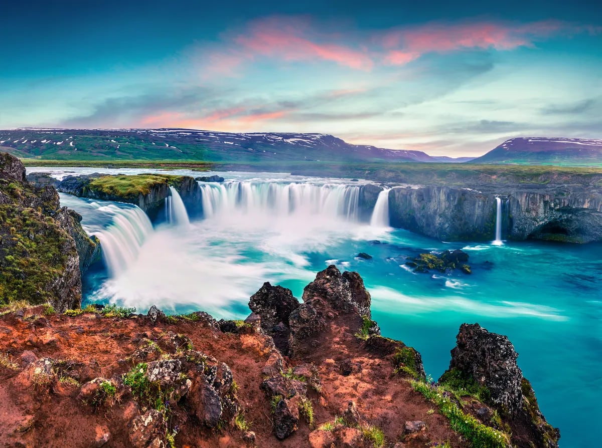 Goðafoss waterfall in North Iceland with turquoise river, lava cliffs and pink sunset clouds, near Húsavík on a scenic road trip