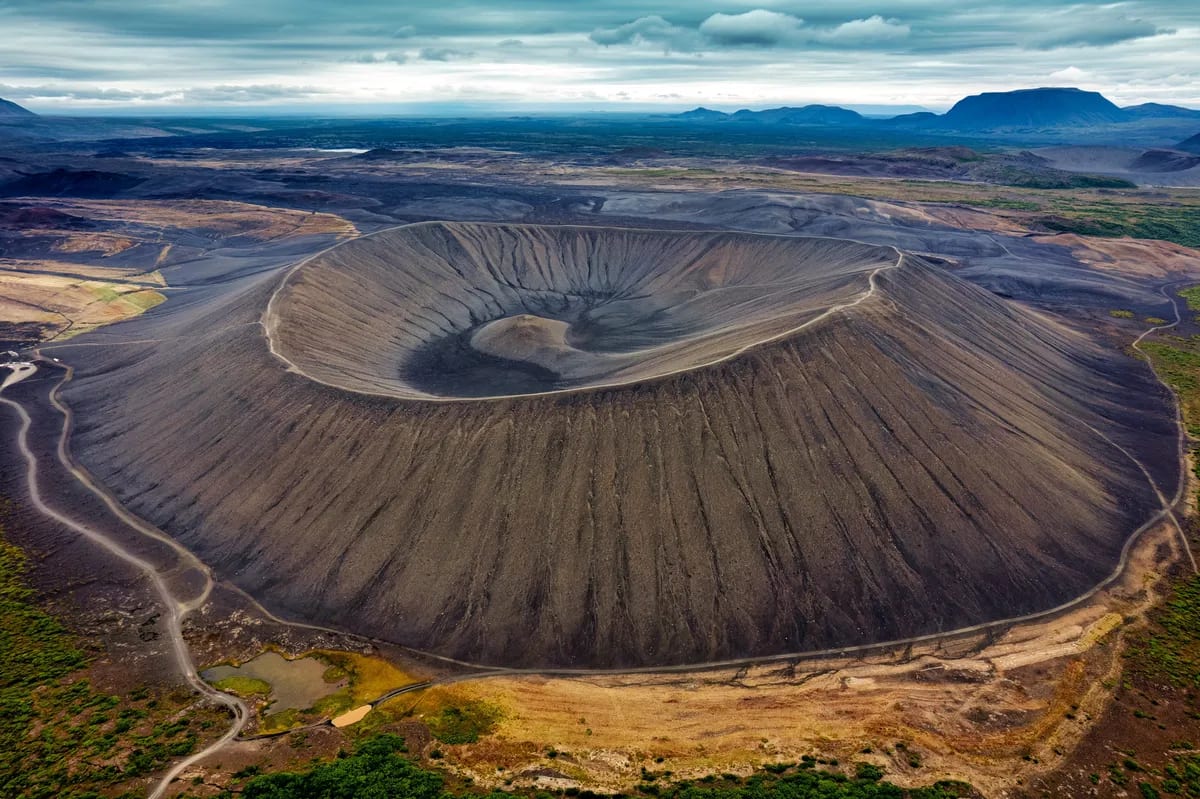 Aerial view of Hverfjall crater near Lake Mývatn in North Iceland, with dark volcanic slopes, winding trails and distant mountains