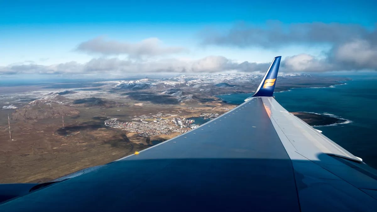 Airplane wing above Reykjavik and Iceland’s coast, with snow-capped mountains, blue ocean and clouds during the flight back home