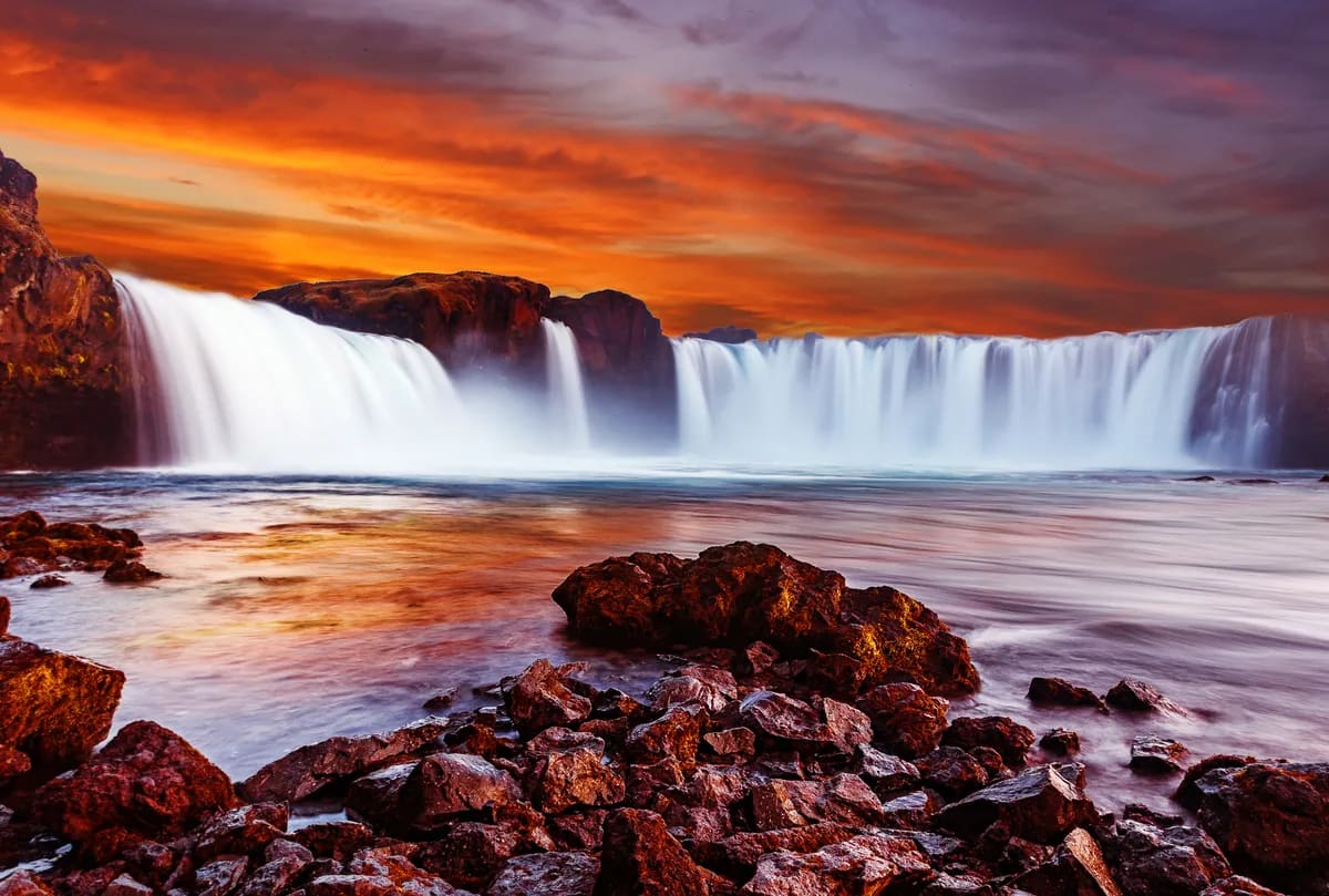 Goðafoss Waterfall at fiery sunset in North Iceland, with silky cascades, misty river, and volcanic rocks for a history guide