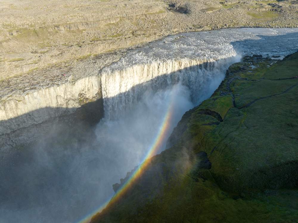 Aerial view of Dettifoss Waterfall in Iceland with a vivid rainbow rising through mist as glacial water crashes into a canyon