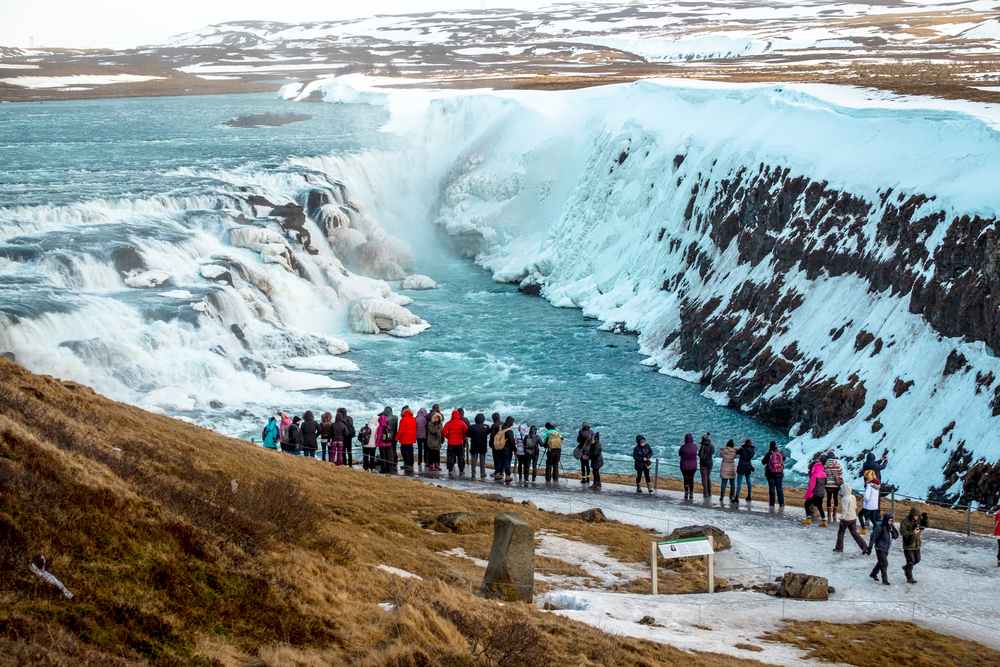 Winter view of Gullfoss Waterfall in Iceland, with snowy canyon walls, icy Hvítá River cascades and tourists on the overlook trail