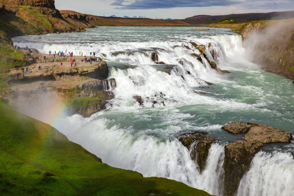 Gullfoss Waterfall in Iceland with roaring Hvítá River cascades, misty canyon, rainbow spray and tourists on the rocky overlook