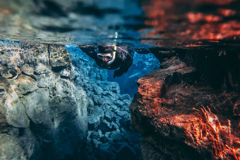 Snorkeler floating through Silfra fissure in Thingvellir National Park, between lava rock walls and crystal-clear glacial water in Iceland
