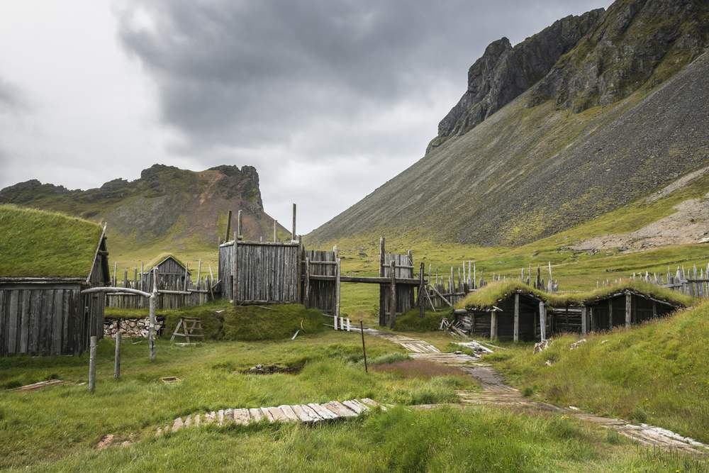 Viking village turf-roof huts near Vestrahorn in southeast Iceland, set in a green valley beneath rugged mountains and cloudy November skies