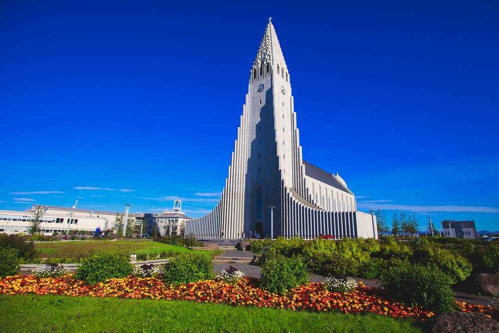 Hallgrimskirkja church in Reykjavik under clear blue sky, with colorful flowerbeds and gardens around Iceland’s iconic landmark