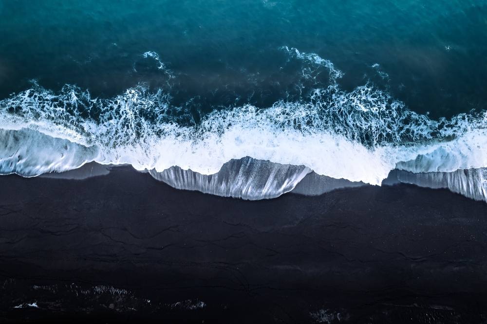 Aerial view of white Atlantic waves breaking on Iceland’s black sand beach, creating dramatic coastal patterns for a November road trip