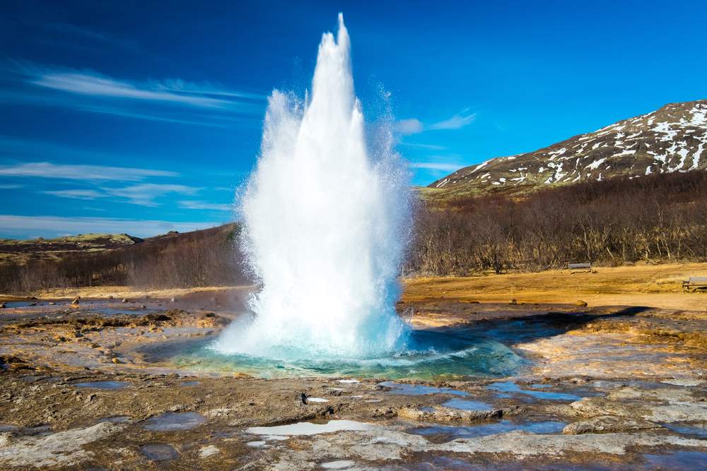 Strokkur geyser erupting in Iceland’s Geysir geothermal area, with steaming blue water, snowy hills and clear skies on a November trip