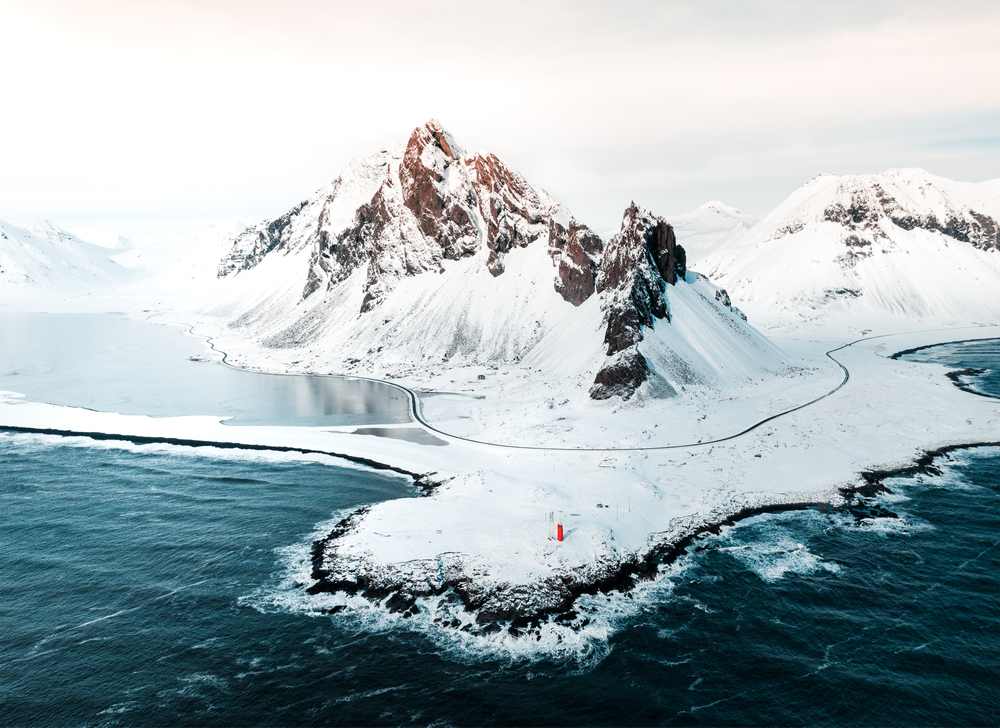 Snow-covered Vestrahorn mountains on Iceland’s coast with icy roads and waves, showing dramatic winter scenery for the best time to visit Iceland