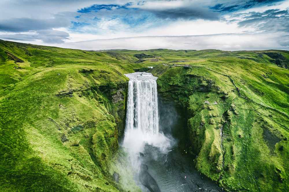 Skogafoss waterfall cascading through lush green summer hills in South Iceland, showing why warmer months are ideal for Iceland road trips