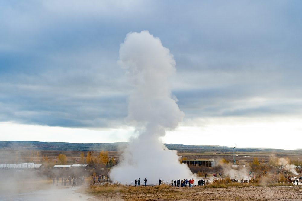 Strokkur geyser erupting in Iceland’s Golden Circle, with steam rising above visitors and autumn colors during an October travel guide