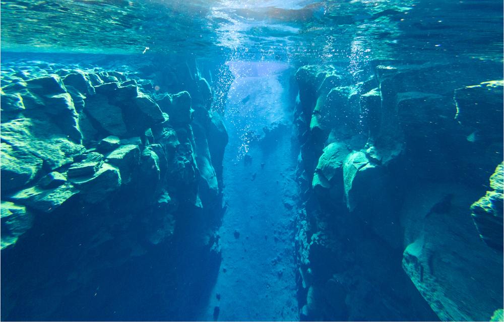 Crystal-clear blue water inside Silfra fissure, with underwater lava rock walls between tectonic plates in Thingvellir National Park, Iceland