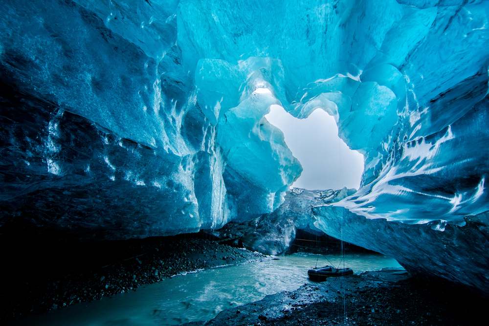 Blue glacier ice cave in Iceland with turquoise frozen walls, meltwater stream, and rocky floor, a top winter adventure near Vatnajökull