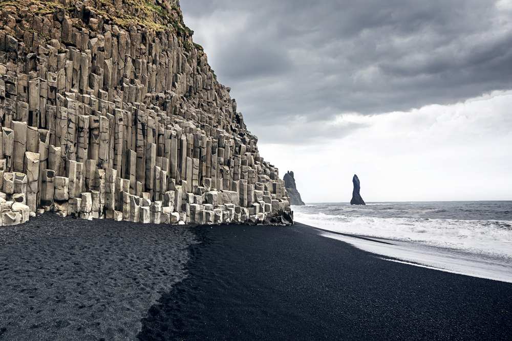 Basalt columns at Reynisfjara black sand beach in Iceland, with volcanic shore, Atlantic waves, Reynisdrangar sea stack and stormy sky