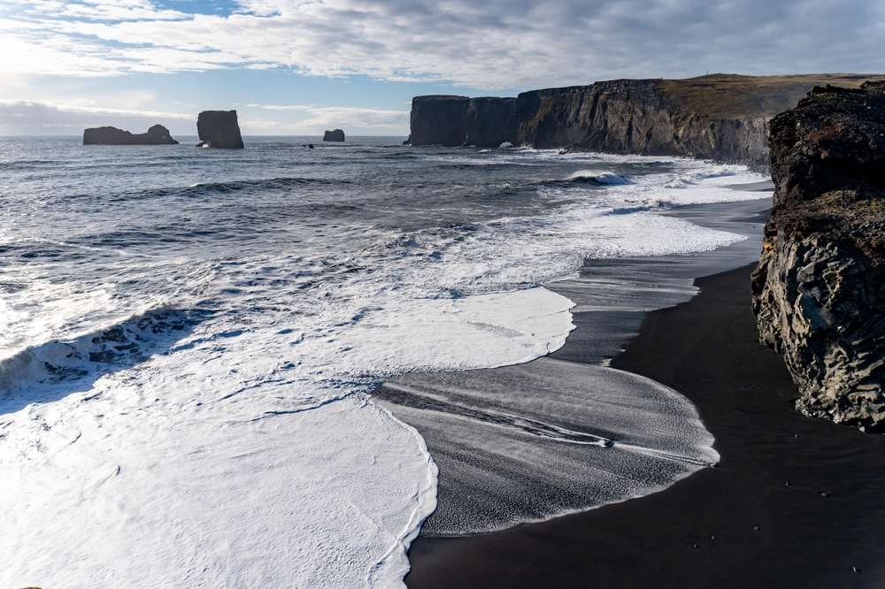 Dyrhólaey viewpoint over Reynisfjara black sand beach in Iceland, with Atlantic waves, volcanic cliffs and offshore sea stacks near Vík