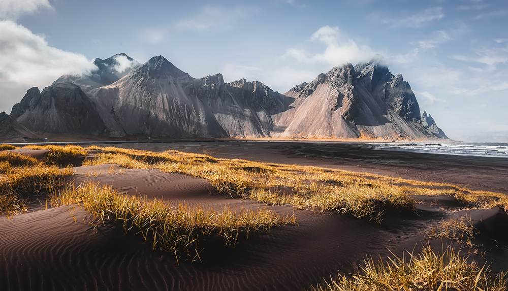 Vestrahorn mountains above Stokksnes black sand beach in Iceland, with grassy volcanic dunes, Atlantic waves and dramatic clouds