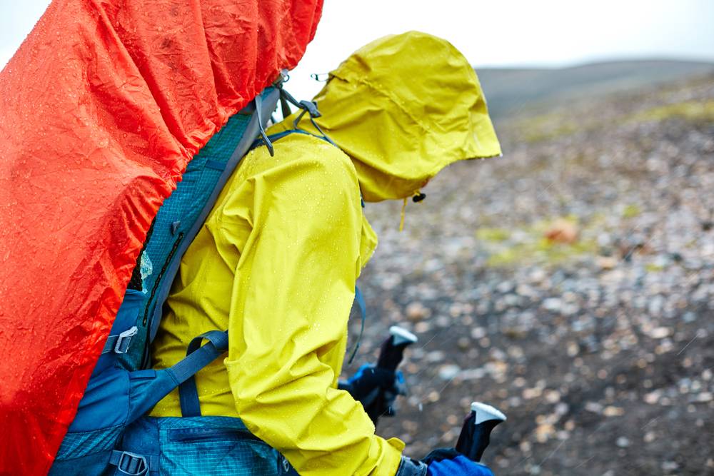 Hiker in yellow rain gear with backpack and trekking poles on a rocky Iceland trail, showing summer weather and outdoor adventure essentials