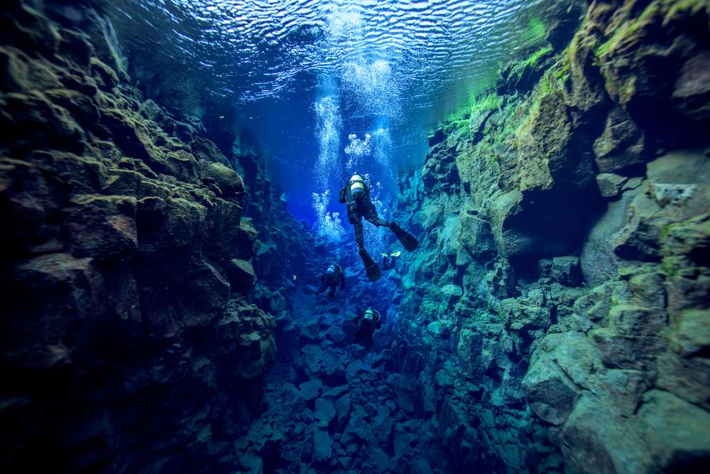 Scuba divers exploring Silfra fissure’s clear blue water between volcanic rock walls in Thingvellir National Park, Iceland in July