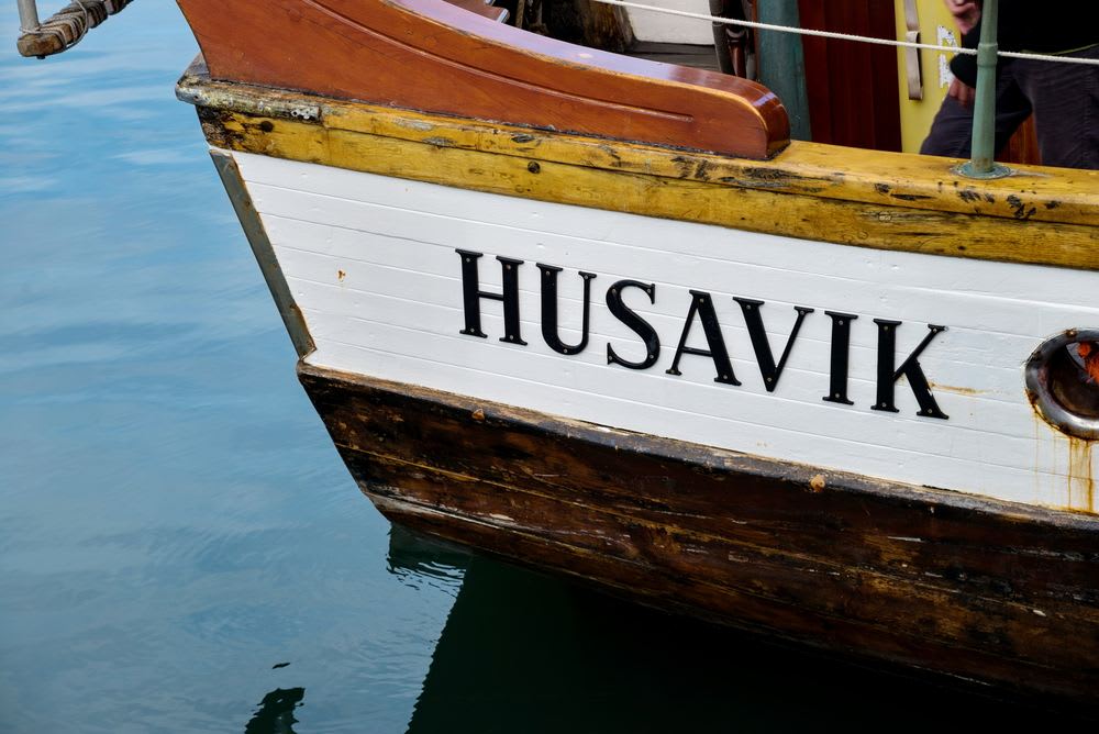 Close-up of a traditional wooden whale-watching boat marked Húsavík, floating in calm harbor water before a tour in northern Iceland.