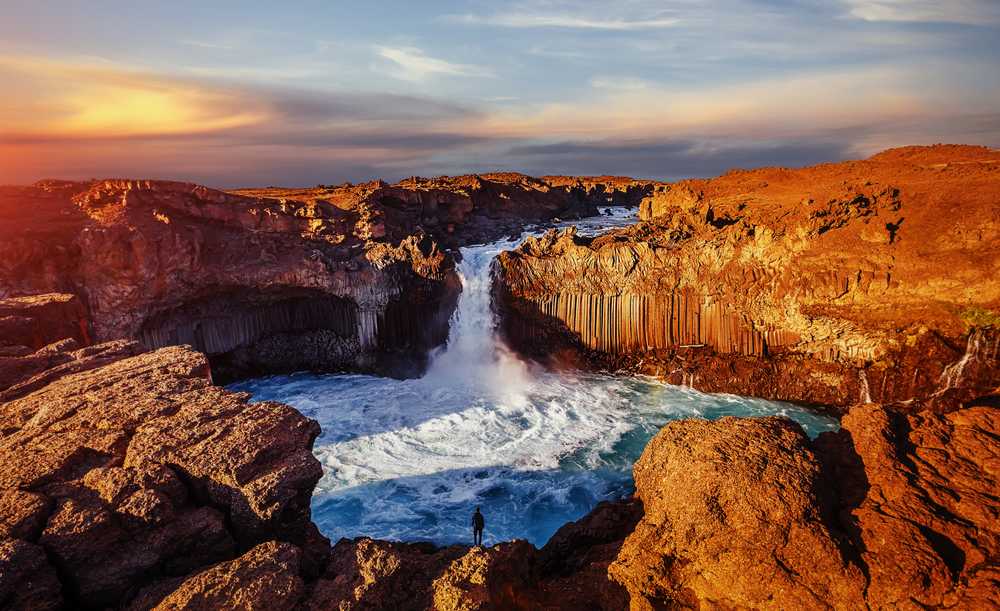 Aldeyjarfoss waterfall plunging into a turquoise pool at sunset, framed by dramatic basalt columns and rugged volcanic cliffs in North Iceland.