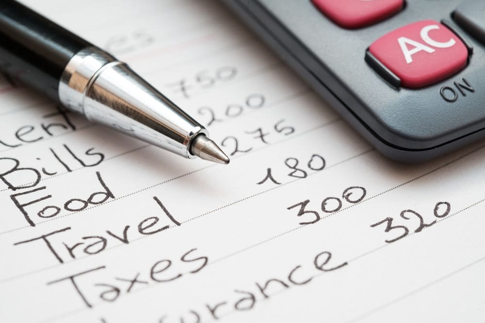 Calculator and pen beside a handwritten budget listing bills, food, travel and taxes, illustrating the expenses of planning a trip to Iceland.