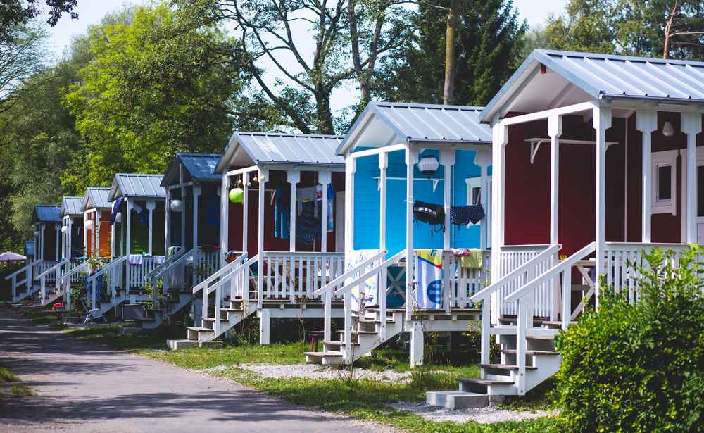 Colorful compact cabins with porches lined along a wooded campsite, illustrating budget-friendly accommodation options for a trip to Iceland.