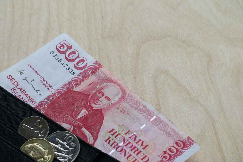Icelandic 5,000 króna banknote and coins tucked into a wallet, illustrating local currency, cash expenses and the cost of traveling in Iceland.