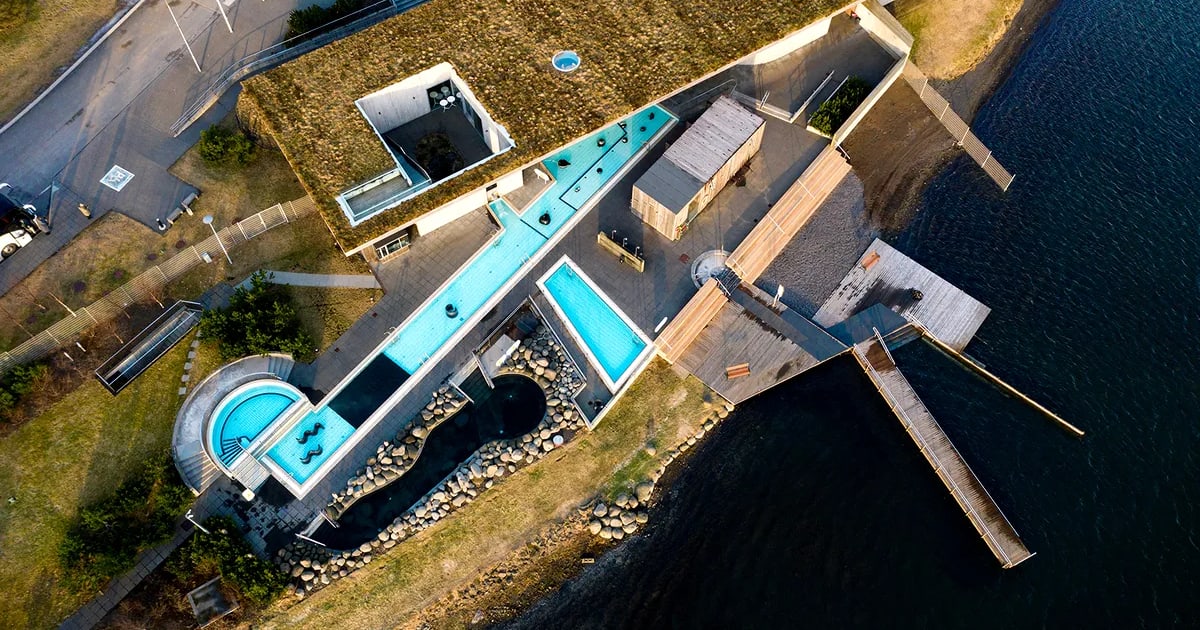 Aerial view of Laugarvatn Fontana geothermal spa with turquoise pools, turf-roofed building, wooden piers and scenic Iceland lake views