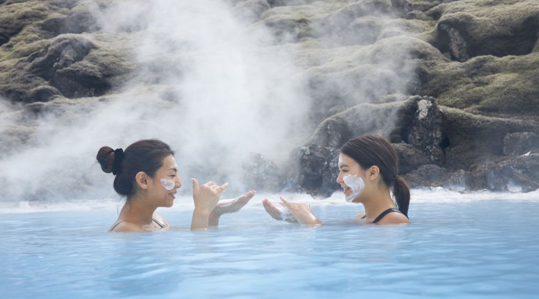 Par de chicas en la Blue Lagoon de Islandia poniendose mascarilla de silica en la cara