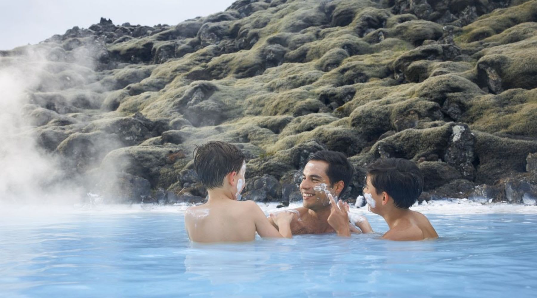 Father and his two children applying a silica face mask in the Blue Lagoon in Iceland.