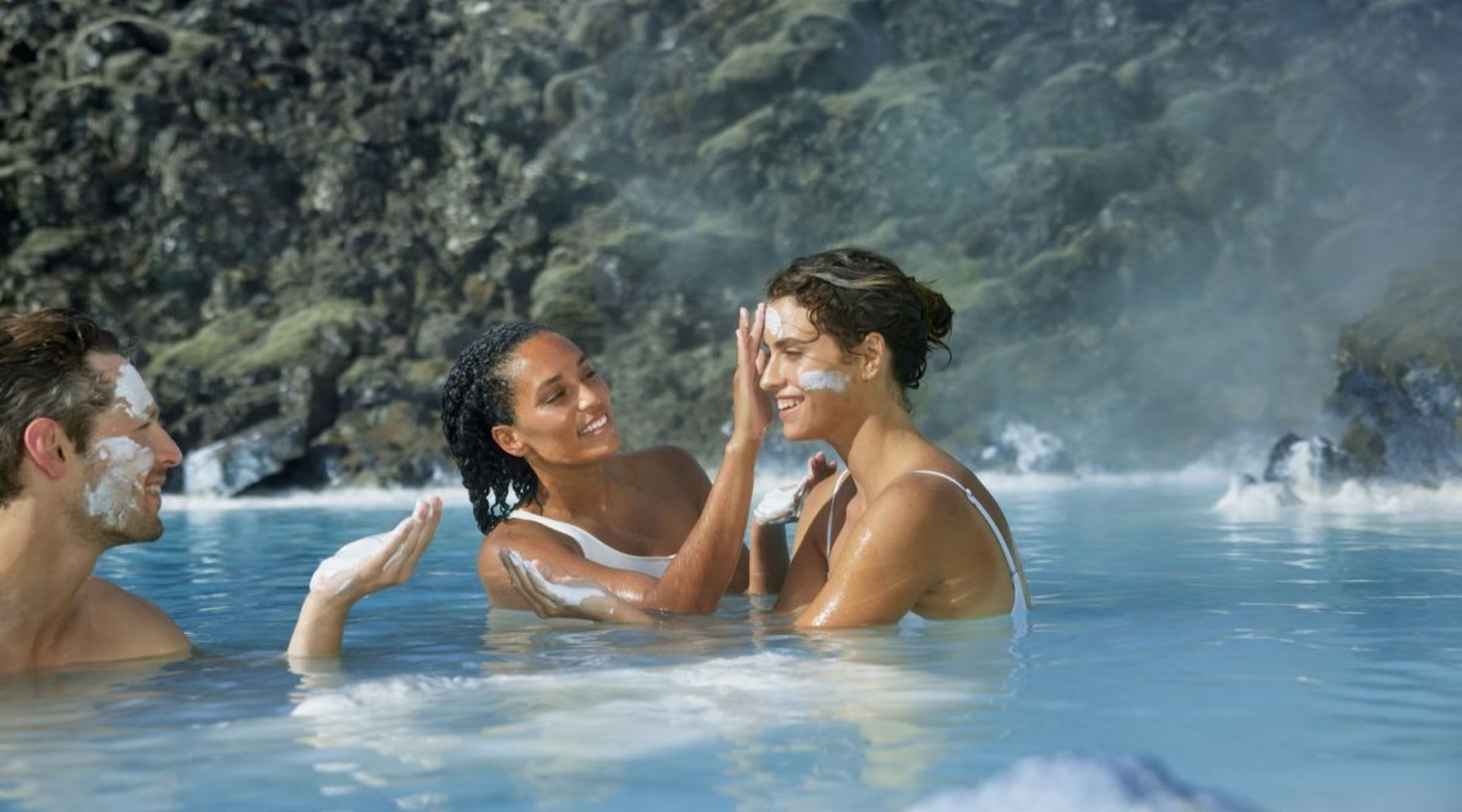Two women applying facial treatment masks in the thermal waters of the Blue Lagoon.