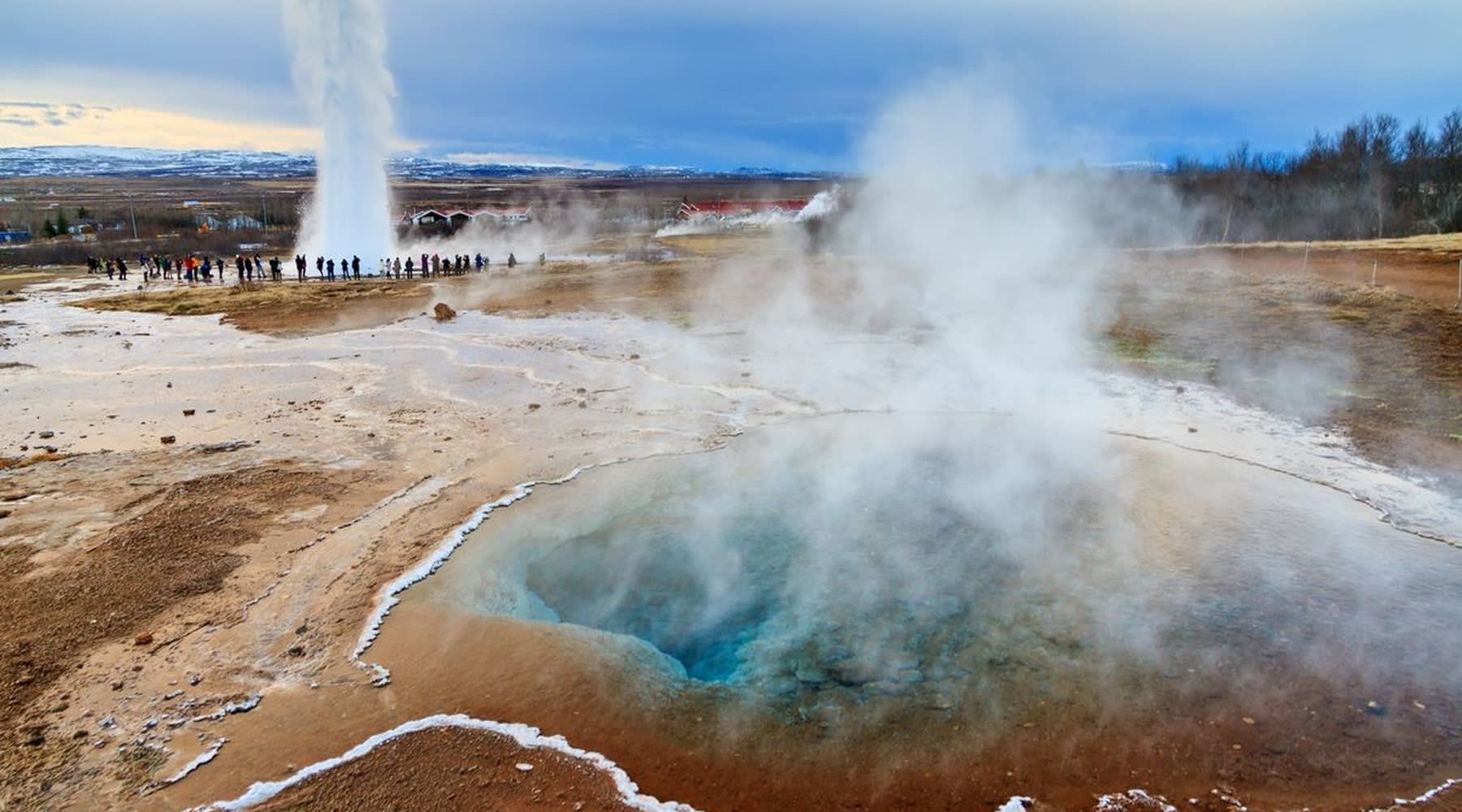 Geothermal area with a geyser erupting and high-temperature pools.