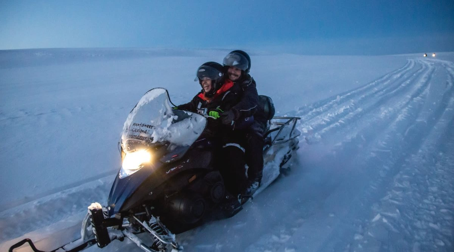 Zwei Touristen auf einem Schneemobil über einen komplett schneebedeckten Gletscher.