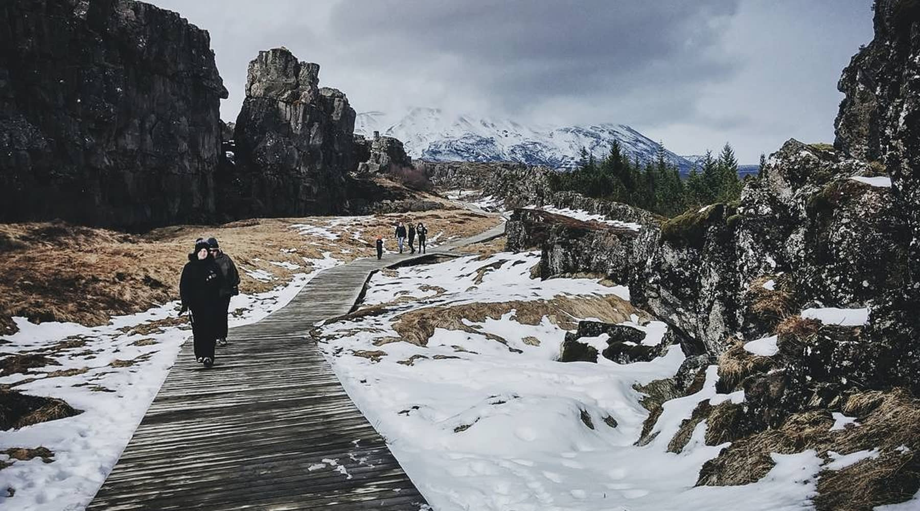 Touristen, die durch den Thingvellir-Park in einer verschneiten Landschaft spazieren.