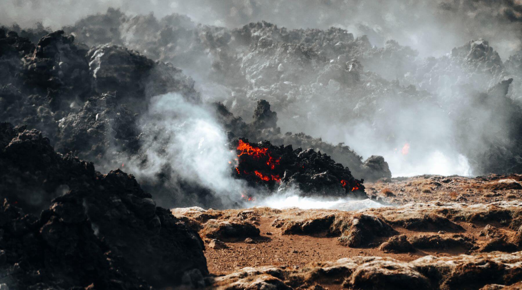 Lava solidifying with constant steam and areas still glowing red hot.