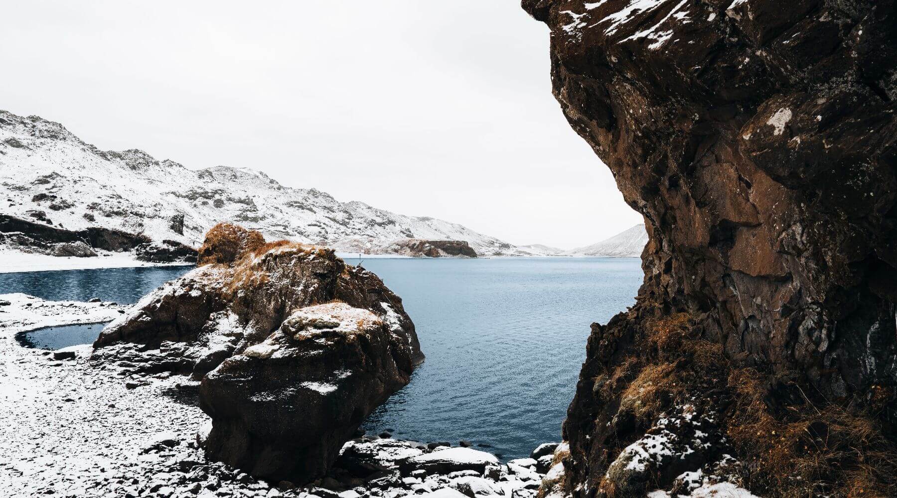 Lava fields covered with snow near a lake.