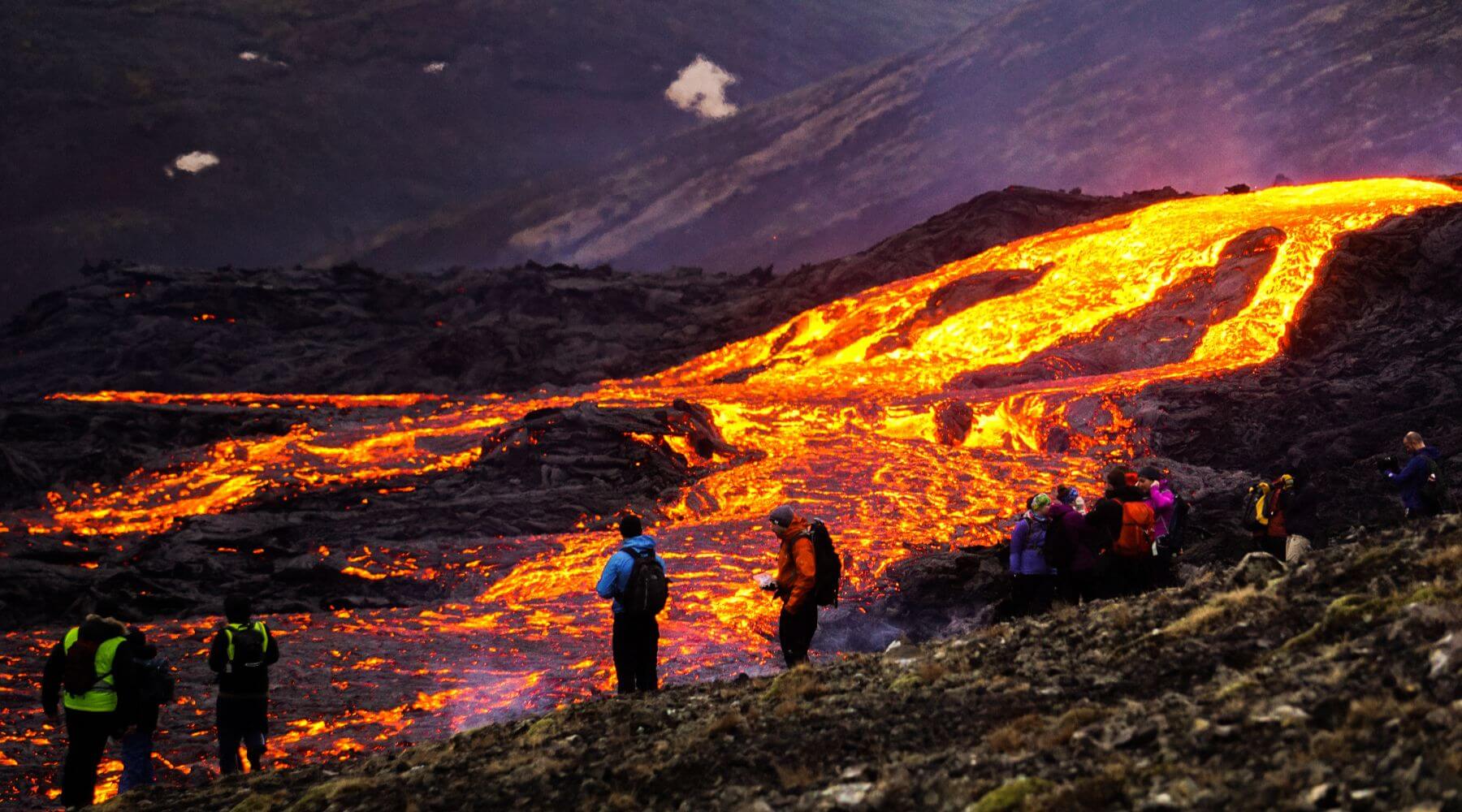 Lava, die die Berghänge hinabfließt, und Touristen, die das Ereignis beobachten.