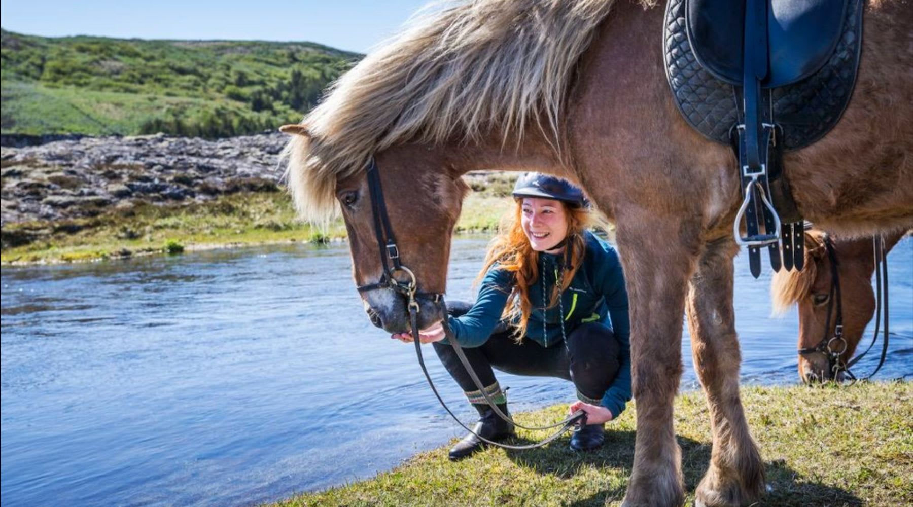 Turista che accarezza il suo cavallo islandese dalla criniera bionda vicino al fiume.